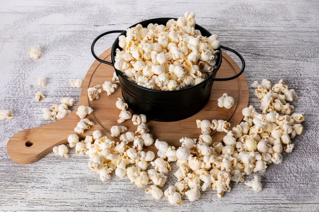 Side view of popcorn in black pan and wooden cutting board on white  horizontal