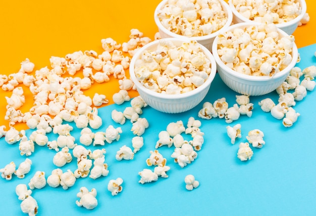 Free photo side view of popcorn in bowls on blue and yellow  horizontal