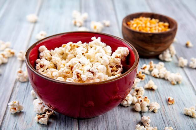 Side view of popcorn on a red bowl with popcorn isolated on grey wood