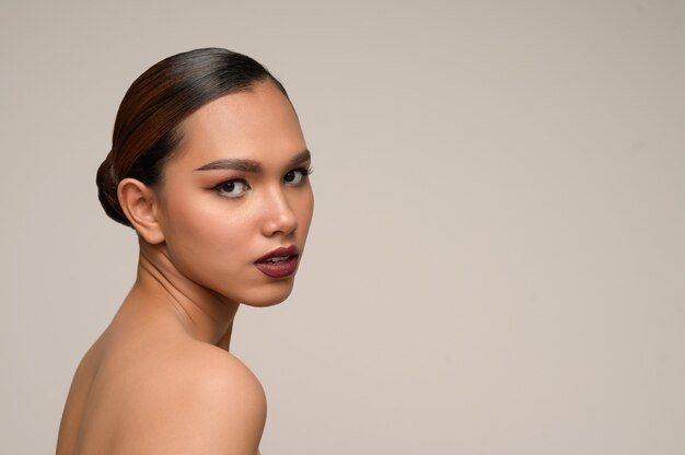 side view portrait of beautiful woman model with fresh daily make-up and perfect smiles with beautiful face on gray wall in studio