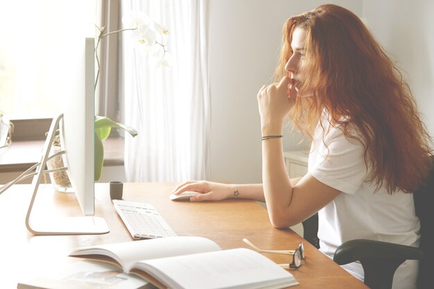 Side view portrait of beautiful young female office worker sitting in front of the computer