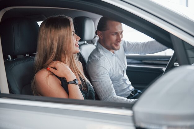 Side view. Positive manager showing features of the new car to female customer