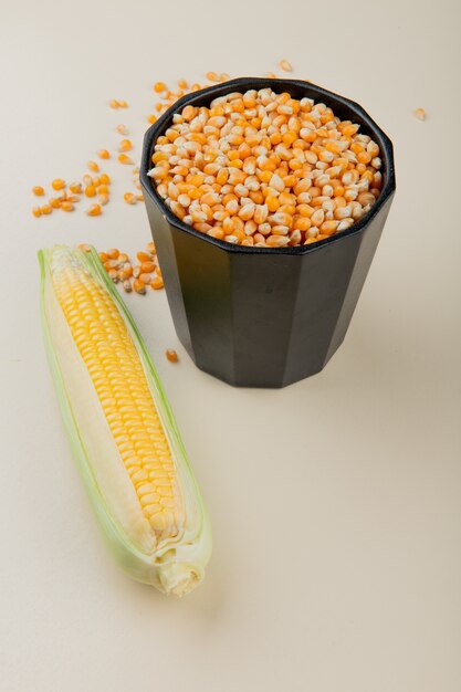 Side view of pot full of corn seeds and corn on white table