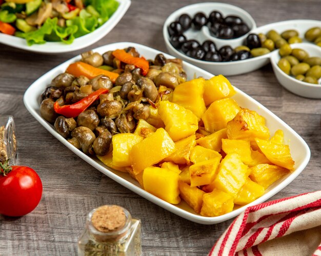 Side view potato with mushrooms and bell pepper on a plate and olives on the table