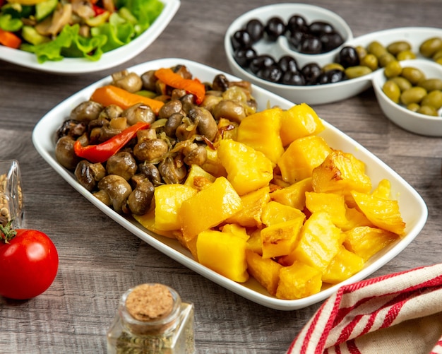 Side view potato with mushrooms and bell pepper on a plate and olives on the table