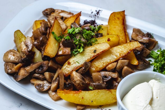 Вид сбоку картофель с жареными грибами картофель с шампиньонами зеленью и сметаной на столе