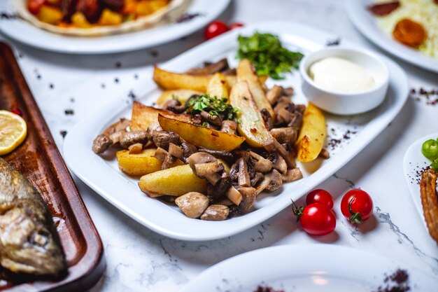 Вид сбоку картофель с жареными грибами картофель с шампиньонами, зеленью, сметаной и помидорами на столе