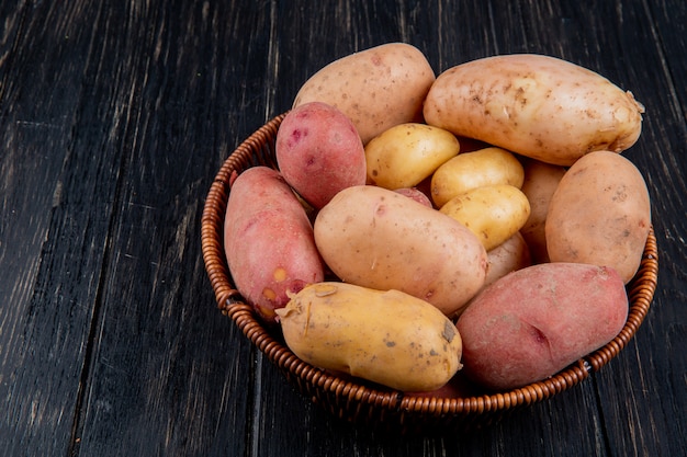 Free photo side view of potatoes in basket on wooden table with copy space