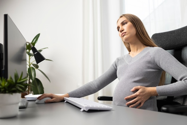 Side view of pregnant businesswoman at her desk holding her belly
