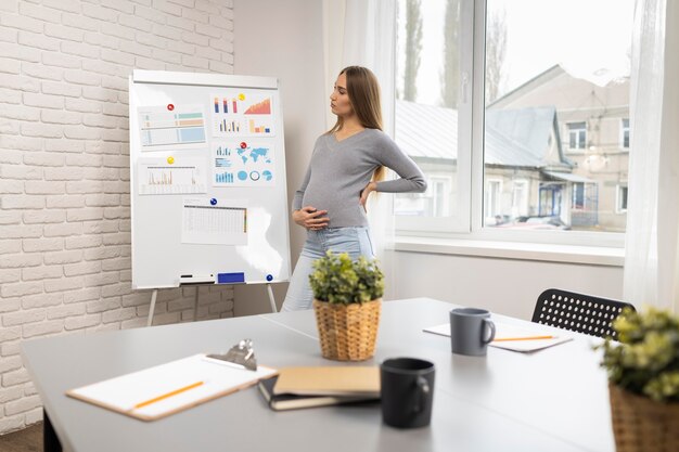 Вид сбоку беременной бизнес-леди с доской в офисе