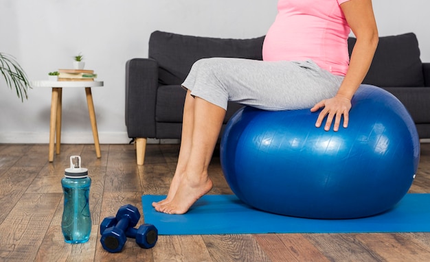 Free photo side view of pregnant woman exercising at home on the floor with ball