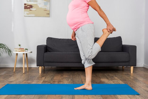 Side view of pregnant woman exercising at home on mat

es
es