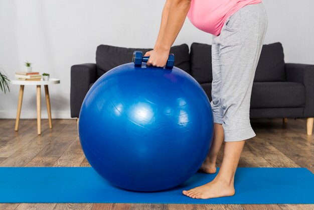 Side view of pregnant woman exercising at home with weights and ball