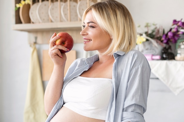 Side view pregnant woman holding an apple