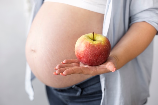 Side view pregnant woman holding an apple