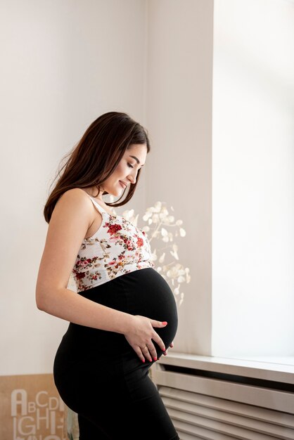 Вид сбоку беременная женщина, держащая ее живот