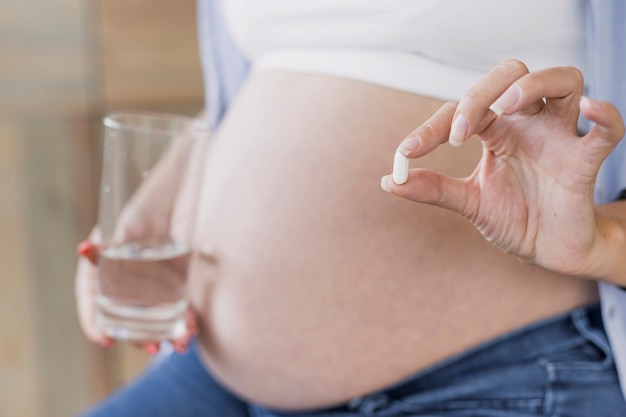 Side view pregnant woman holding a pill