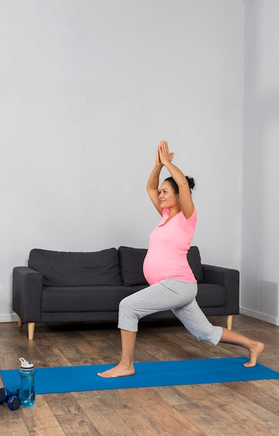 Vista laterale della donna incinta a casa con esercitando la posizione yoga pratica mat