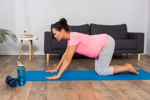 Side view of pregnant woman at home with weights and exercising mat