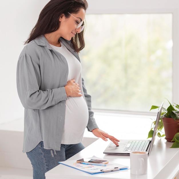 Free photo side view of pregnant woman at home working on laptop