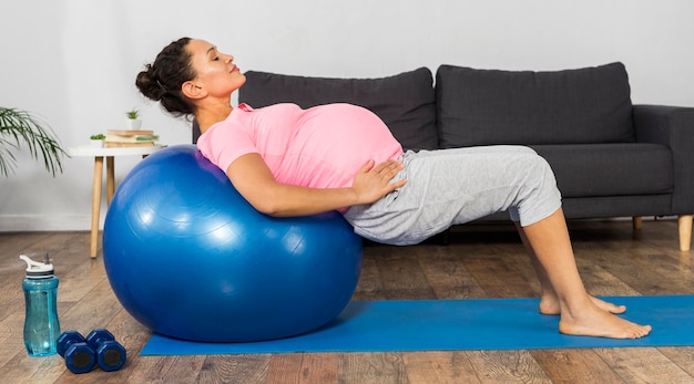 Вид сбоку беременной женщины, использующей мяч для упражнений