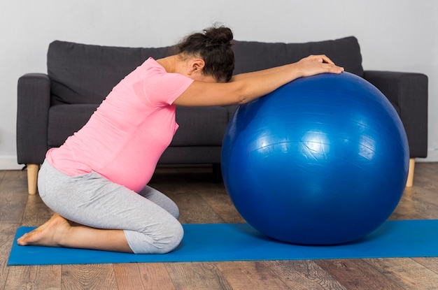 Side view of pregnant woman with ball and exercise mat at home