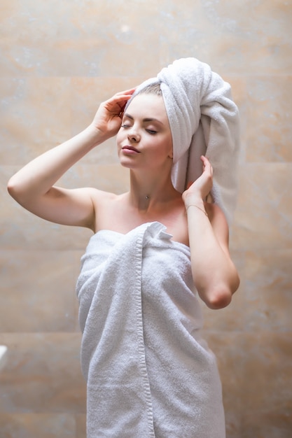 Foto gratuita vista laterale della bella donna con un asciugamano sulla testa e in posa di accappatoio. ritratto di donna con spalla nuda godendo del tempo dopo la doccia fresca. bellezza, concetto di cura della pelle.