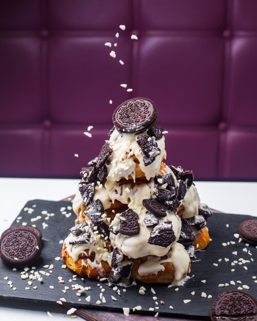 Side view of profiterole decorated with white chocolate and cookies on a wooden board