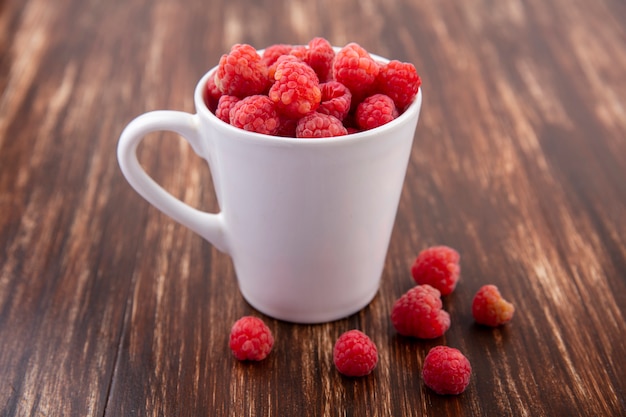 Free photo side view of raspberries in cup and on wood