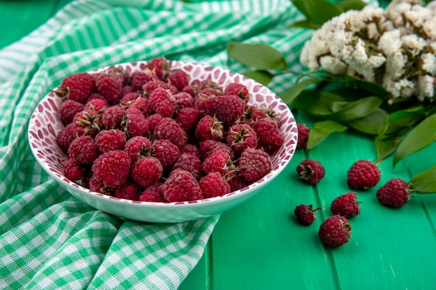 Side view of raspberries on a plate with flowers on a green checkered towel on a green surface