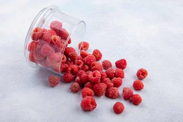 Side view of raspberries spilling out of glass bowl on white