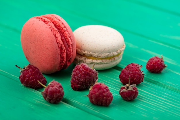 Side view of raspberries with macarons on a green surface