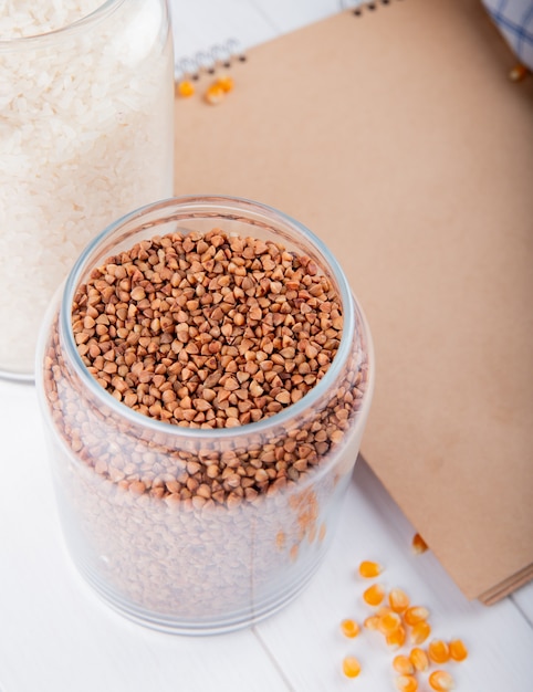 Side view of raw buckwheat in a glass jar on the table with sketchbook