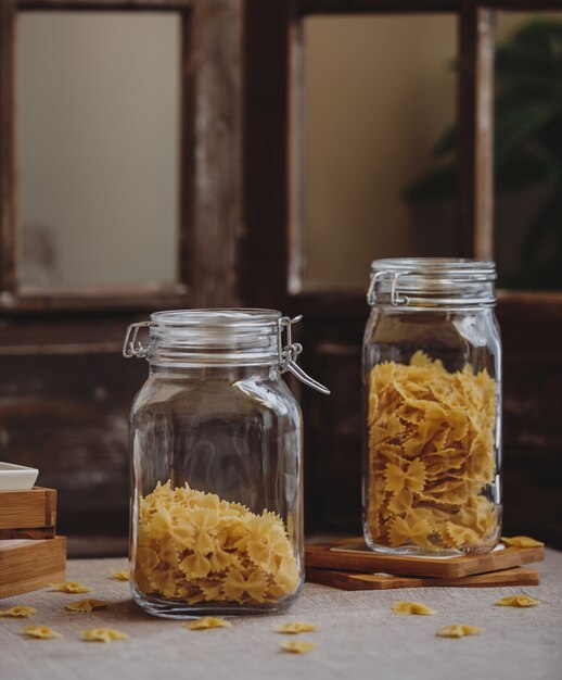 Side view of raw farfalle pasta in glass jars on a wooden table