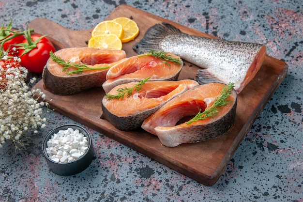 Side view of raw fishes lemon slices greens pepper on wooden cutting board and knife fresh foods on blue black mix colors table