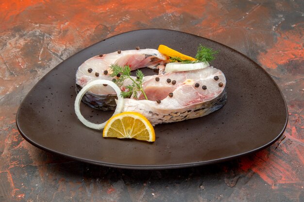 Вид сбоку на сырую рыбу и перец, ломтики лимона, лук на черной тарелке на поверхности смешивания цветов