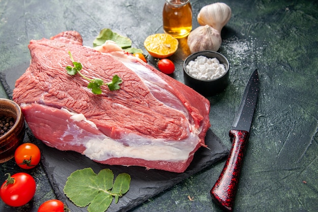 Side view of raw fresh red meat and greens on cutting board knife tomatoes cut lemon oil on green black mix colors background