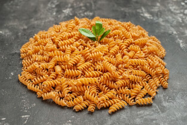 Side view of raw Italian pastas with green arranged in circle on gray background