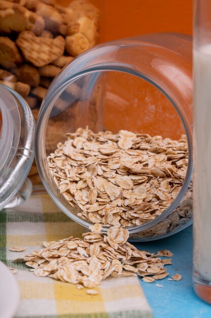 Side view of raw oatmeal flakes scattered from glass jar