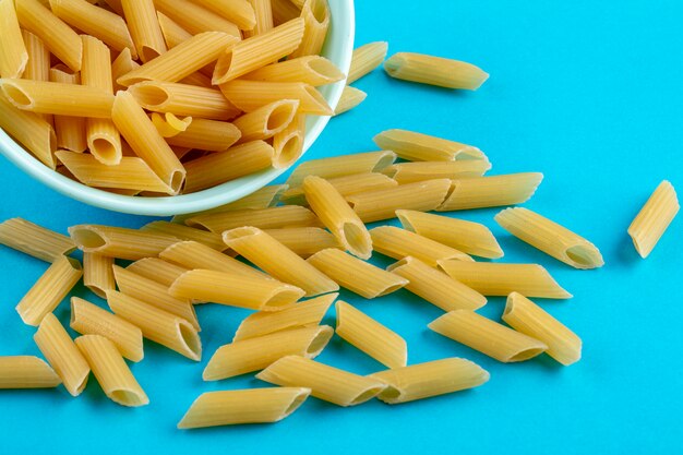 Side view of raw pasta in a saucer on a blue surface