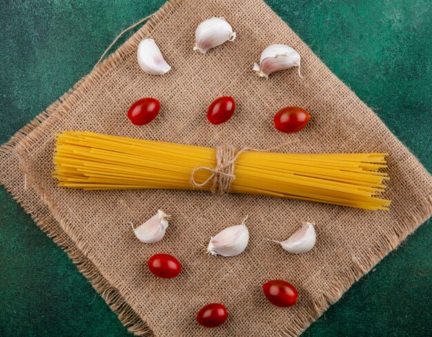 Foto gratuita vista laterale di spaghetti crudi con pomodorini e aglio su un tovagliolo beige