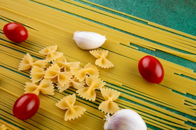 Vista laterale di spaghetti crudi con pasta pomodorini e aglio su una superficie verde