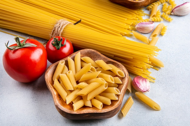 Side view of raw spaghetti with raw pasta in bowls with garlic and tomatoes on a gray surface