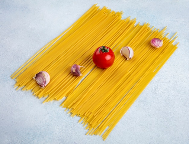 Side view of raw spaghetti with tomato and garlic on a gray surface