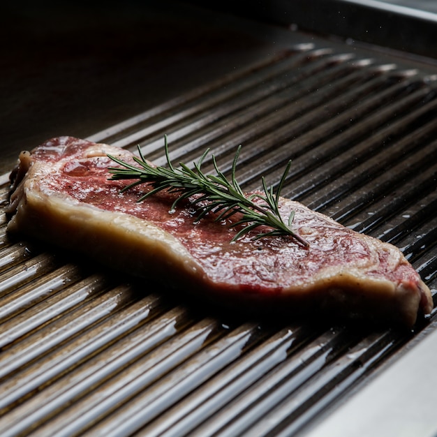 Side view raw steak with barbecue and rosemary