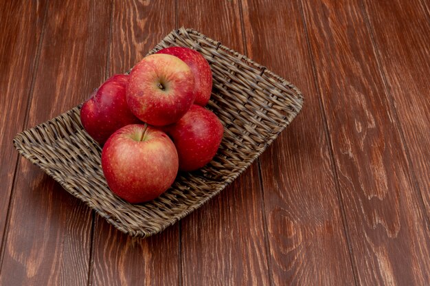Вид сбоку красных яблок в корзине на деревянной поверхности с копией пространства