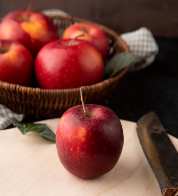 Side view red apples in a basket with an apple and a knife on the board