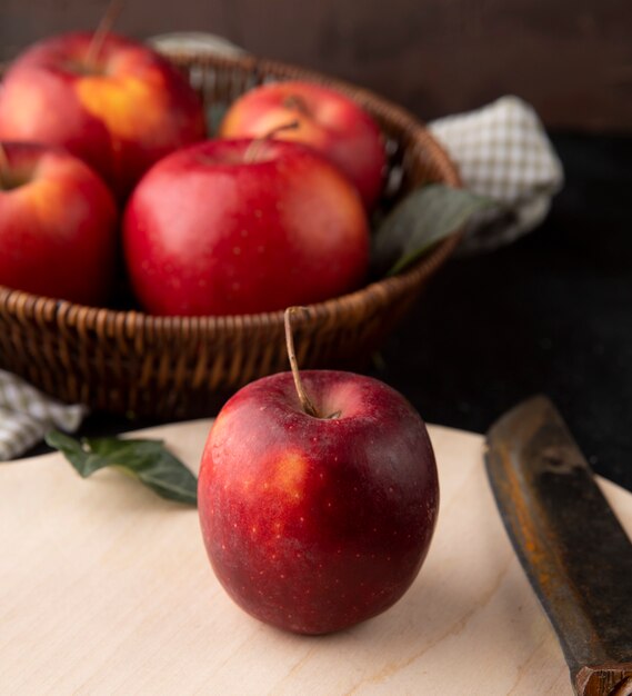 Side view red apples in a basket with an apple and a knife on the board