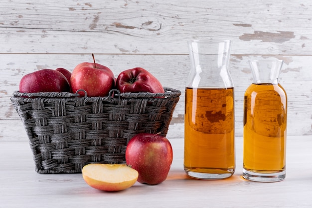 Вид сбоку красные яблоки в корзине с соком на белом деревянном столе