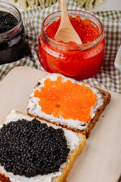 Side view red and black caviar toast rye and white bread with cottage cheese red caviar and black caviar on a board